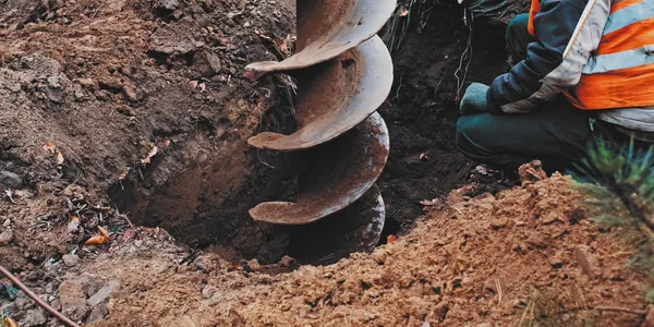 Construction-worker-operating-a-large-earth-auger-drill-in-soil_